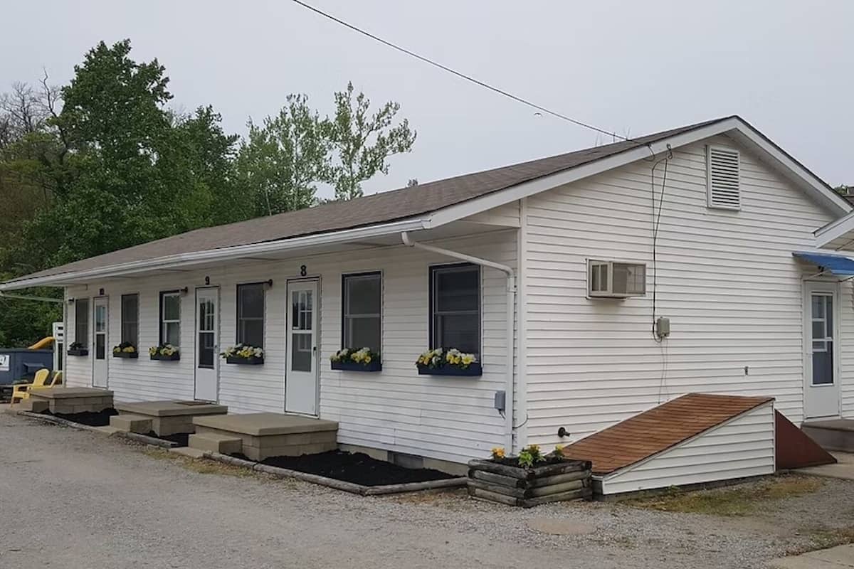 A single-story mobile home with a front porch, a ramp for accessibility, and flower boxes on the windows.