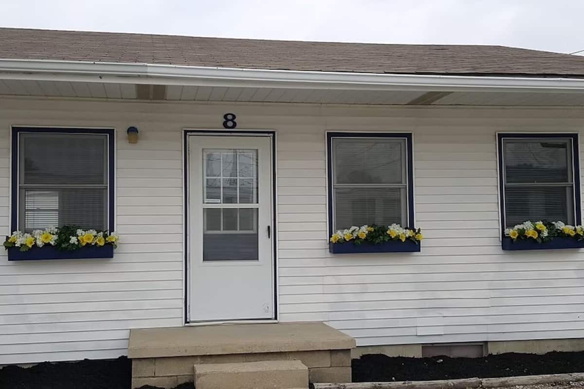 A single-story house with a white exterior, numbered 8, featuring three windows with flower boxes.