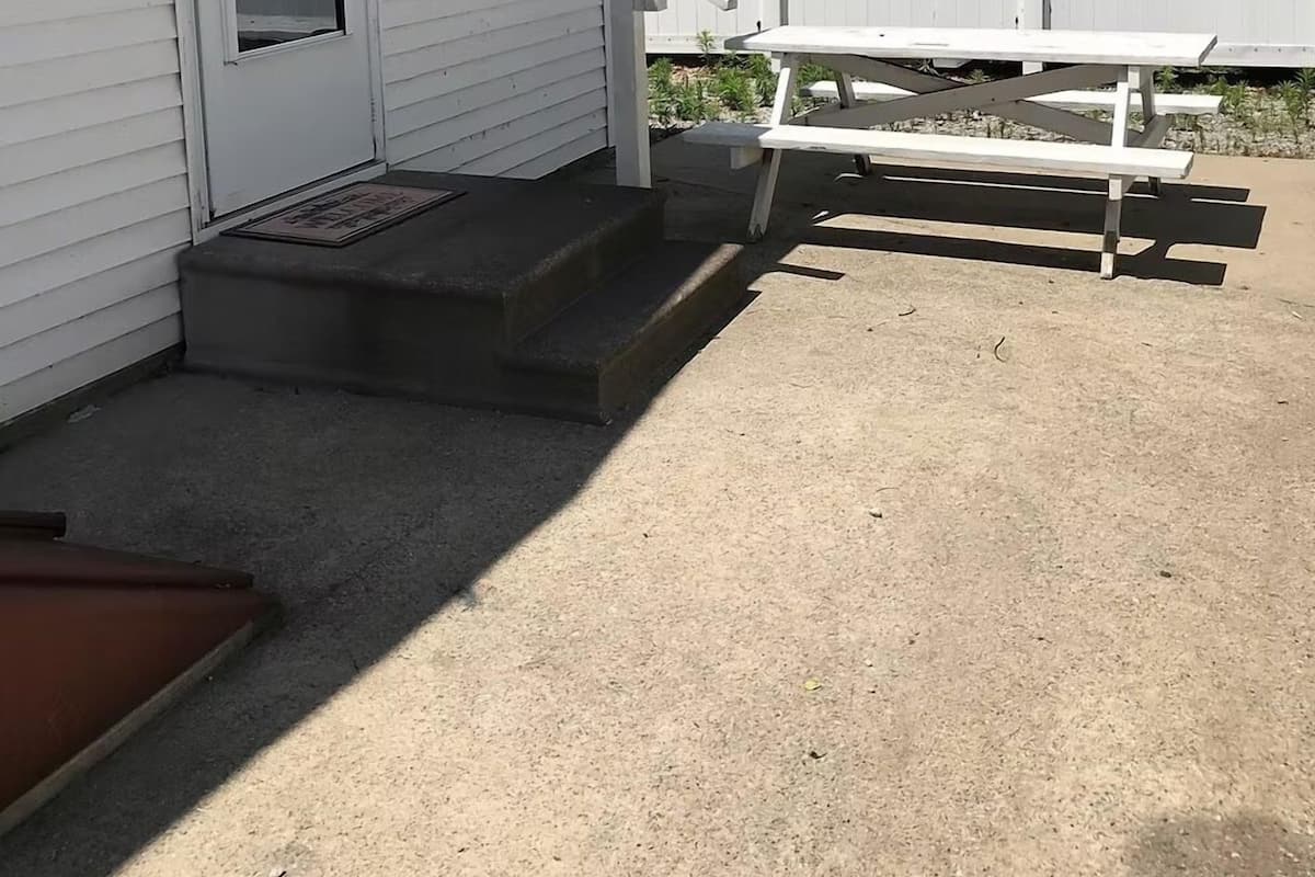 A house with a white exterior, a front door, a small porch with steps, and a picnic table in the backyard.