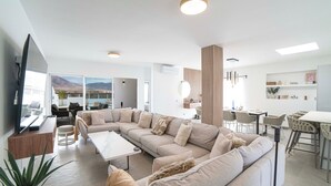 A modern living room with a large sectional sofa, a dining area with a white table, and a kitchen in the background. - Luxury, High-Standard Villa with Hot Tubs, Air Con & Pool - Sleeps 8 (Playa Blanca)