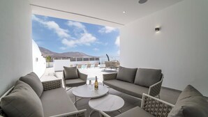 A modern outdoor seating area with a sofa, chairs, and a table, overlooking a pool and mountains. - Luxury, High-Standard Villa with Hot Tubs, Air Con & Pool - Sleeps 8 (Playa Blanca)
