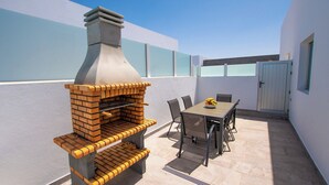 Un patio al aire libre con una barbacoa de ladrillo, una mesa con sillas y una puerta al fondo.