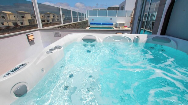 Un jacuzzi con vista a una piscina y edificios al fondo.