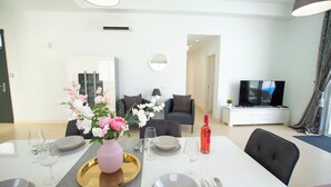 Una sala de estar moderna con comedor, televisor y un amplio ventanal con cortinas.