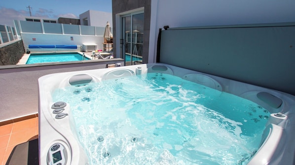 Boblebad med kontrolpanel, swimmingpool og en bygning med store vinduer i baggrunden.