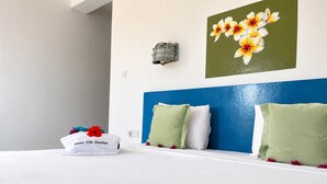 Habitación de hotel con cama, almohadas, una lámpara fijada a la pared y un cuadro con motivos florales.