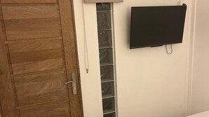 Un dormitorio con puerta de madera, televisor montado en la pared y cama con ropa blanca.