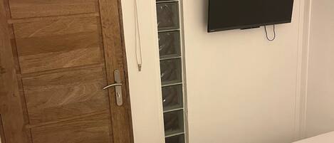 Un dormitorio con puerta de madera, televisor montado en la pared y cama con ropa blanca.