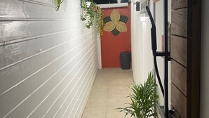 Un pasillo estrecho con paredes blancas, una puerta roja y una planta en maceta.