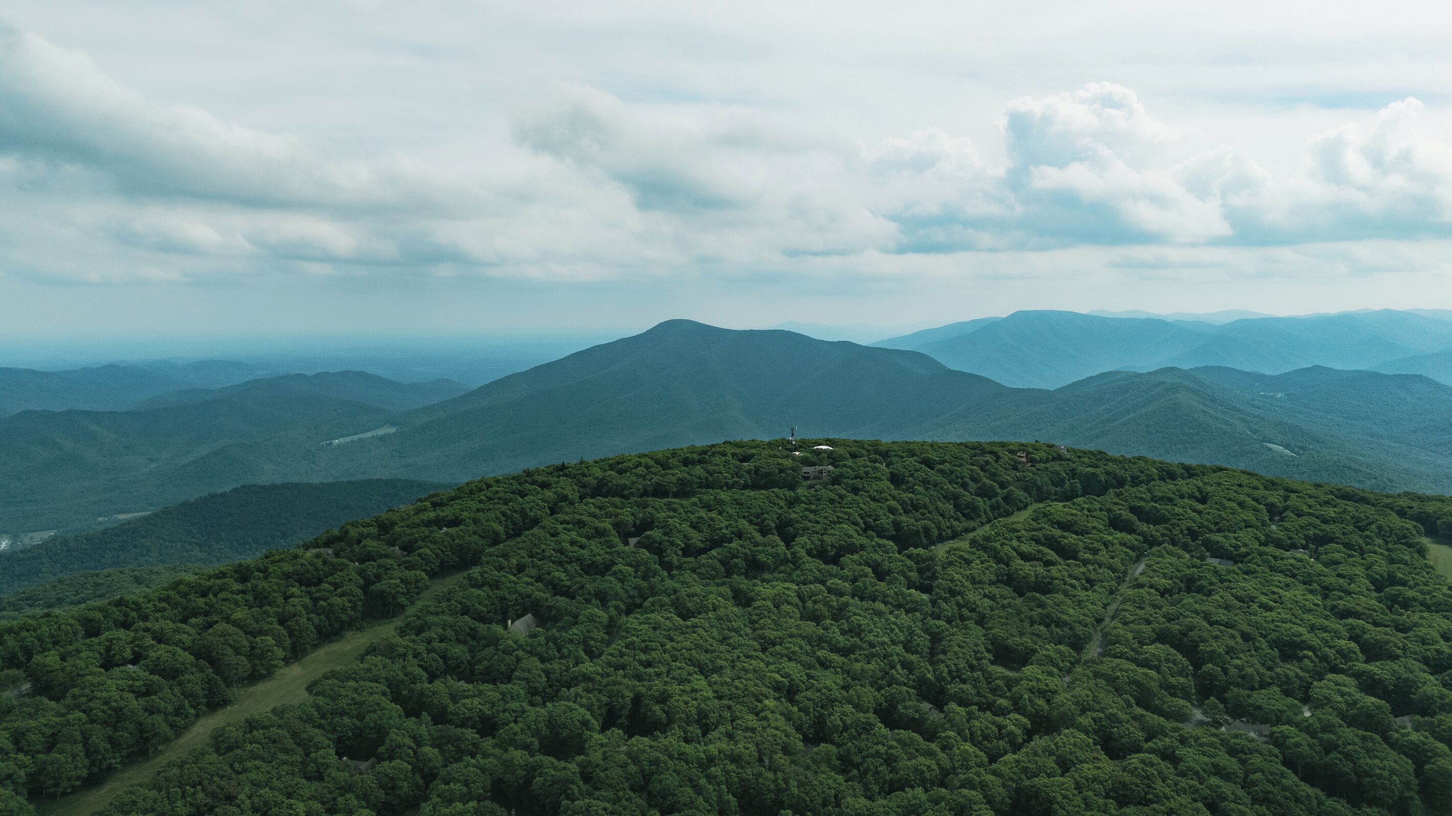 A mountainous landscape with dense forest and a few buildings.