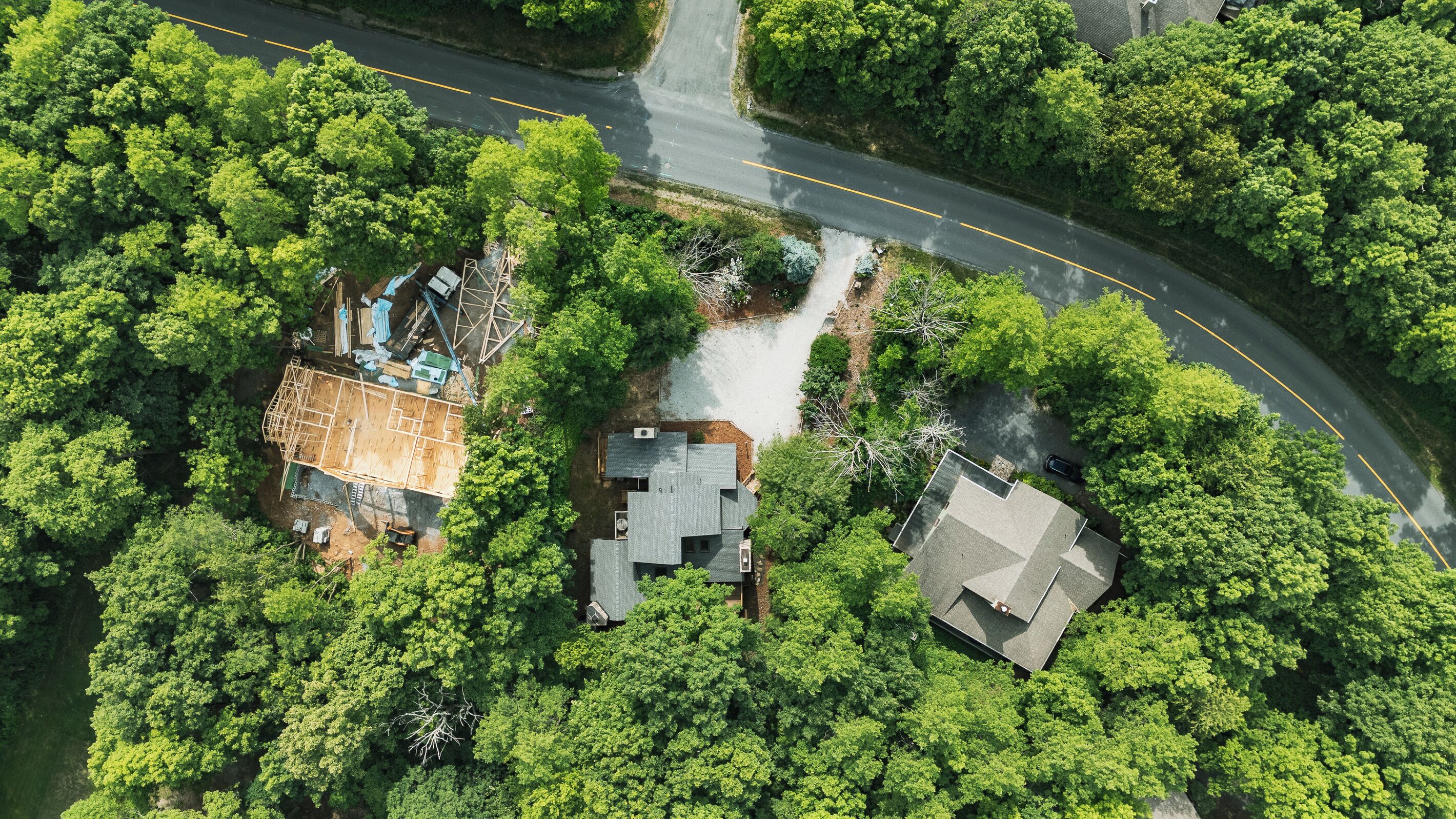 Luchtbeeld van een woongebied met huizen, omgeven door weelderige begroeiing, een kronkelende weg en een bouwterrein.