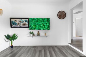 A modern living room with a wooden floor, a green wall art, a clock, and a small shelf with decorative items.