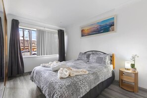 A bedroom with a patterned bedspread, a bedside table with a lamp, and a window with curtains.