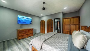 Ein Schlafzimmer mit einem Bett, einem Holzschrank, einem an der Wand montierten Fernseher und einem Deckenventilator.