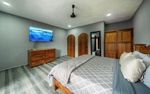 Un dormitorio con cama, armario de madera, televisor en la pared y ventilador de techo.