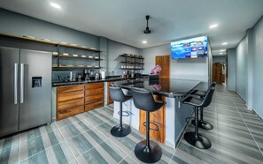 Una cocina moderna con una isla central, taburetes de bar, un refrigerador y un televisor de pantalla plana montado en la pared.