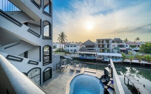 Een resort met een zwembad, een steiger met boten en uitzicht op de ondergaande zon boven een kustplaats.