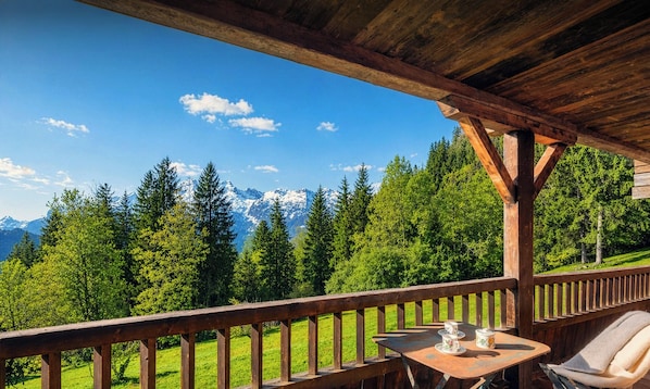 Una terraza de madera con una mesa y sillas, con vistas a un paisaje montañoso.
