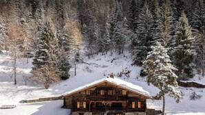Eine Holzhütte mit schneebedecktem Dach, umgeben von Bäumen und verschneiter Landschaft.