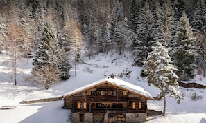 Una cabaña de madera con techo cubierto de nieve, rodeada de árboles y un paisaje nevado.