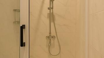 Una ducha con paredes de vidrio, un cabezal de ducha manual y un grifo empotrado.