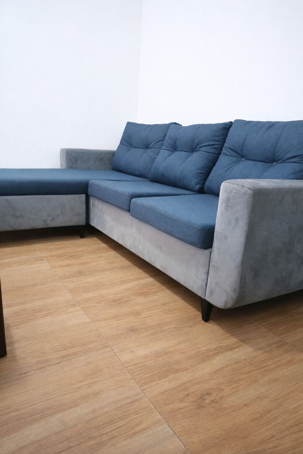 Un sofá seccional gris con chaise, piso de madera y pared blanca lisa.