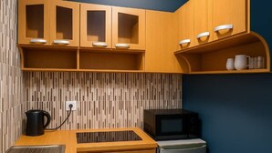 A compact kitchen with wooden cabinets, a microwave, a small refrigerator, and a kettle. - CJ Apartment  (Kasoa)