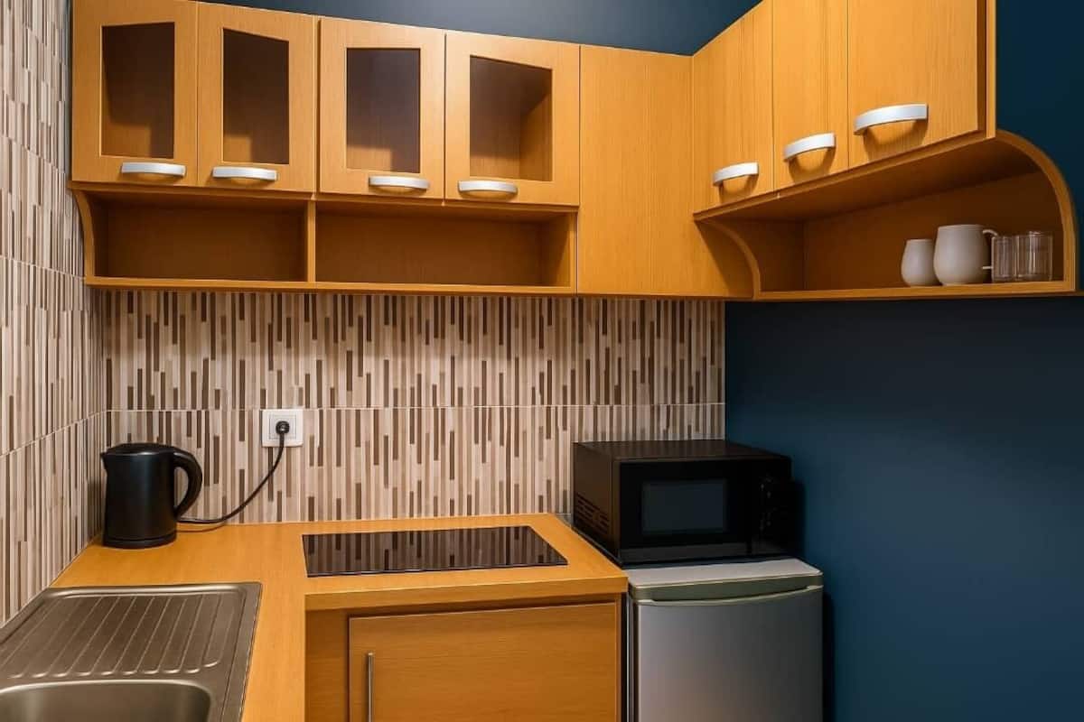 A compact kitchen with wooden cabinets, a microwave, a kettle, and a refrigerator.