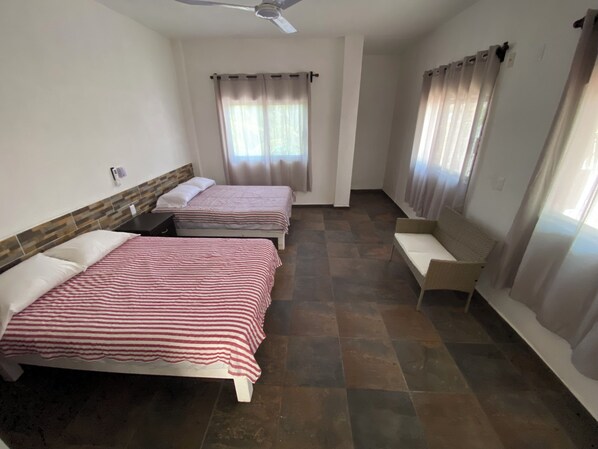 A room with two beds, a ceiling fan, a sofa, and a window with curtains. - Very comfortable suite with 2 dbl beds, terrace and AC. Only 2 blocks from beach (Los Ayala)