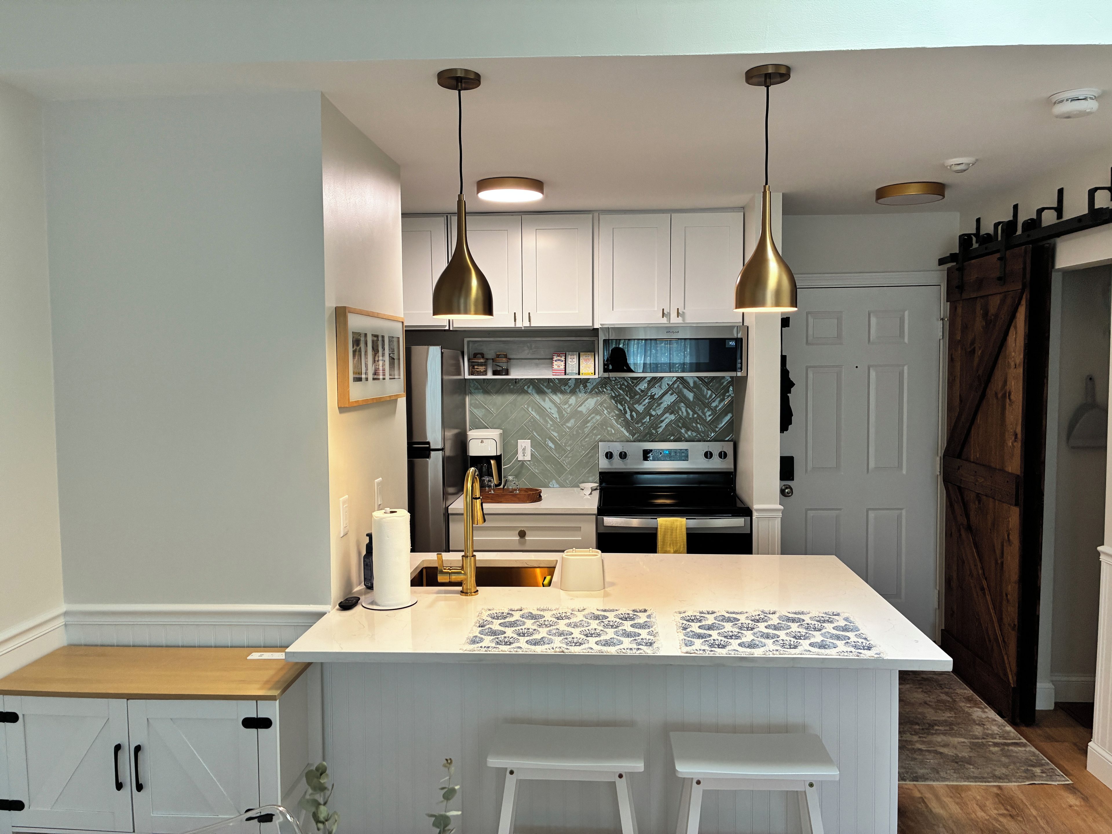 Een moderne keuken met witte kasten, een centraal eiland met barkrukken, roestvrijstalen apparatuur, hanglampen en een decoratieve spatwand.