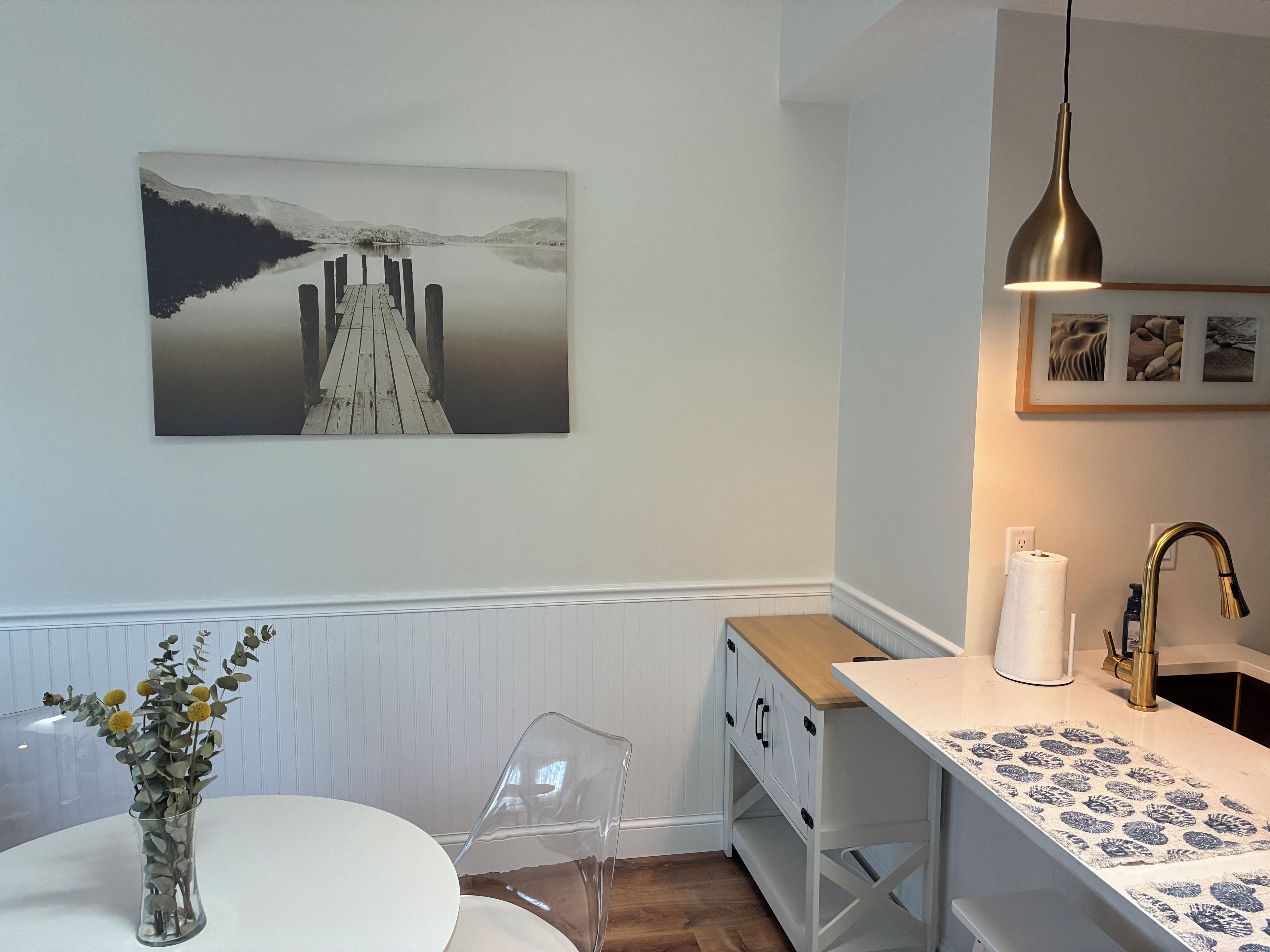 A modern kitchen with a wooden countertop, a clear vase with flowers, and a painting of a pier.
