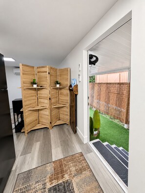 A room with a sliding wooden partition, a black cabinet, a small plant, and a door leading to a green outdoor area. - Quiet Modern Studio • Full kitchen in Dania Beach (Hollywood)