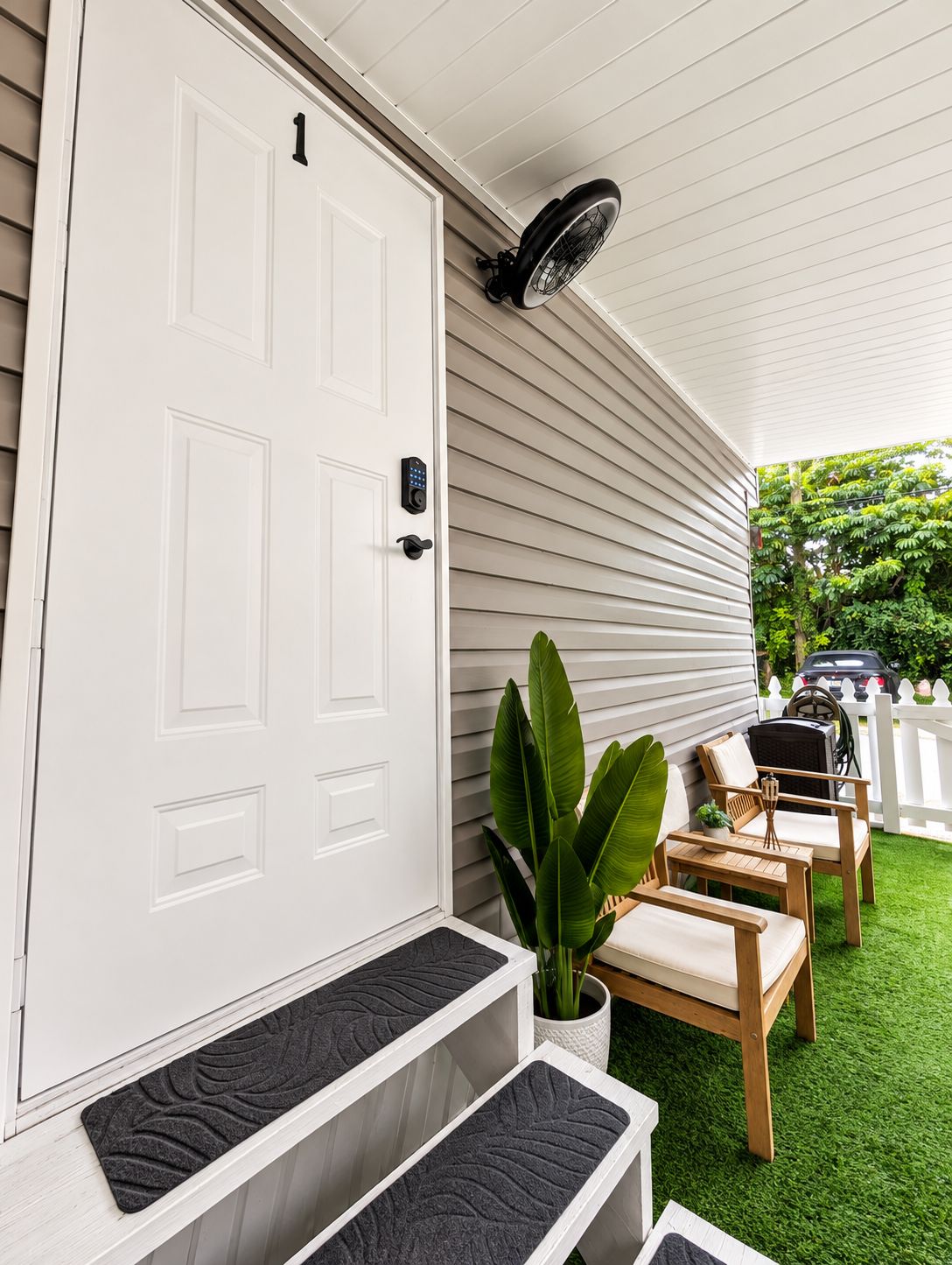 A white door with a number 1, a porch with a fan, and a small table with chairs.