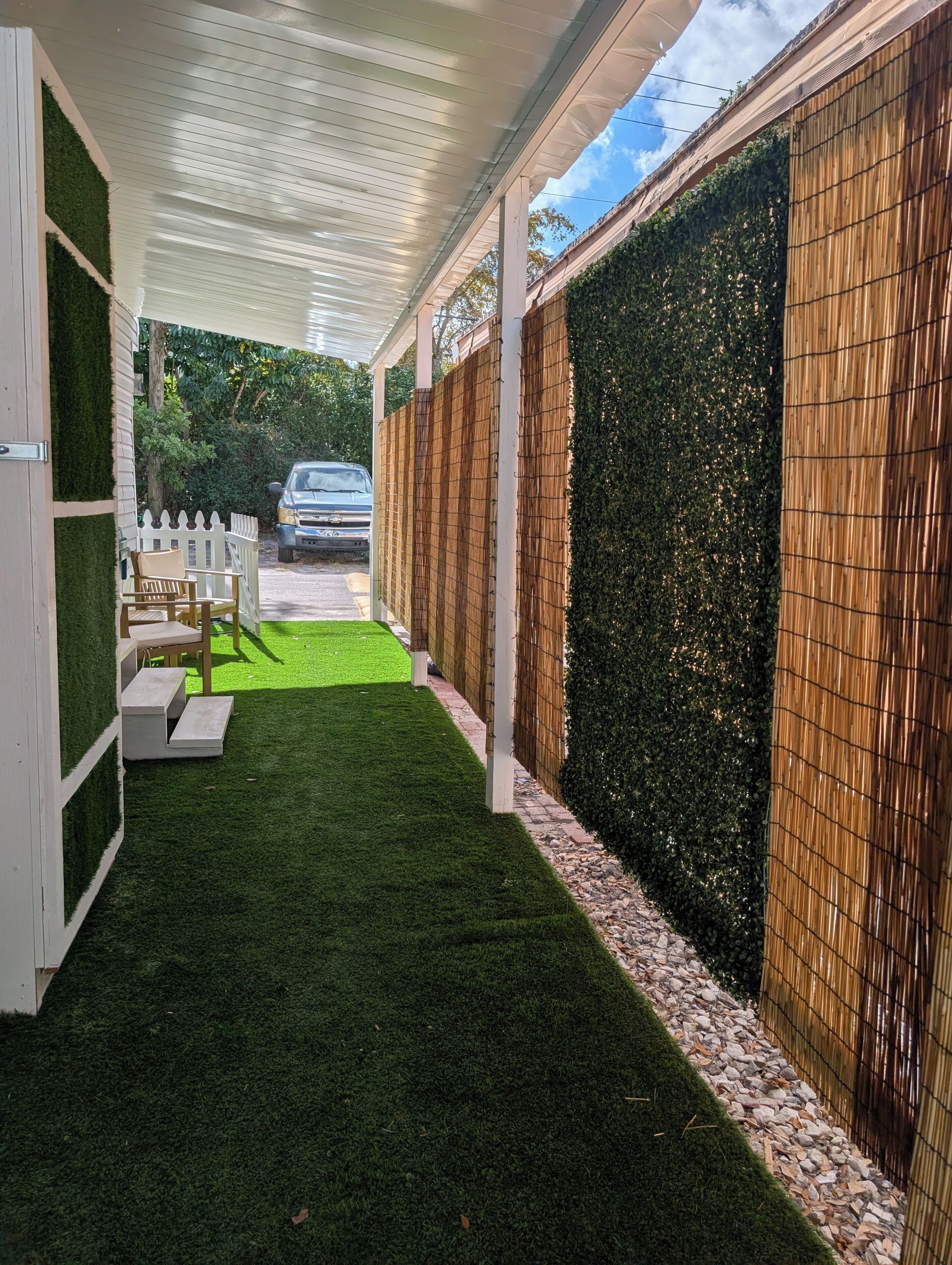 A covered outdoor area with artificial grass, a white fence, and a bamboo wall.