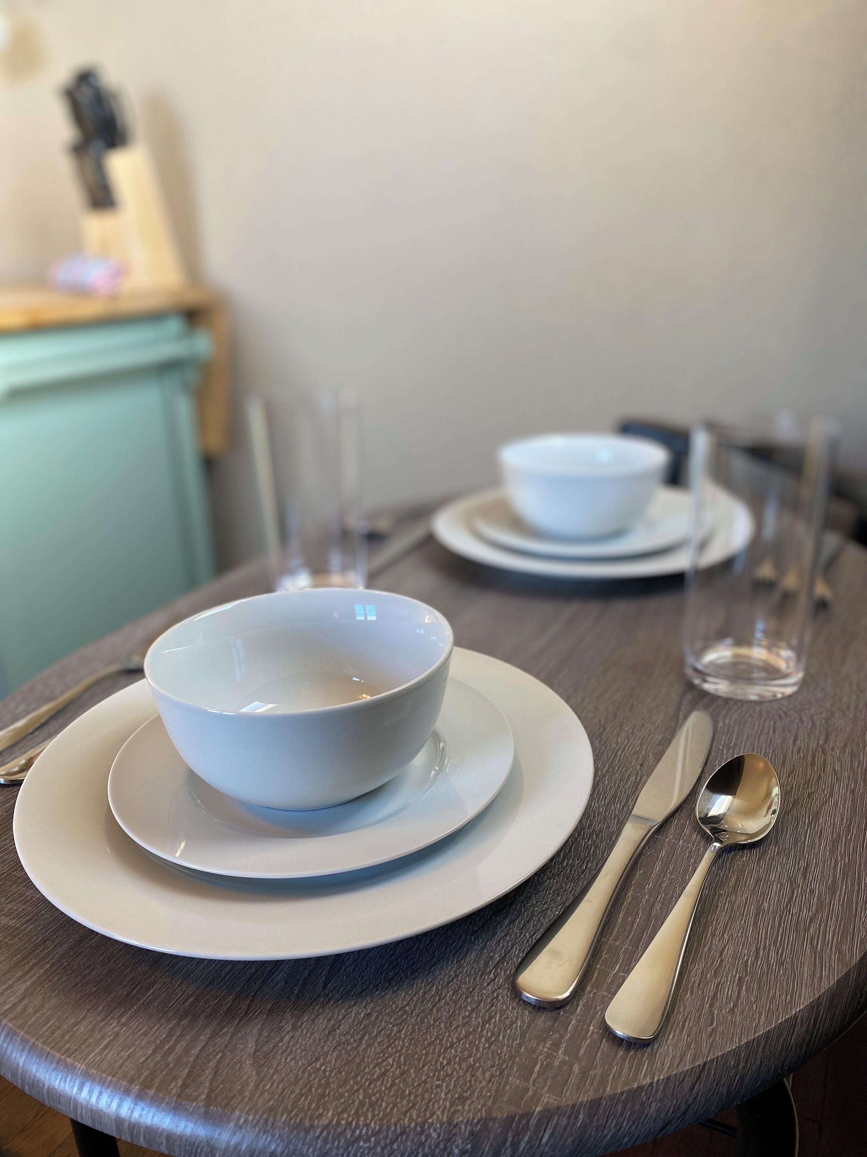 A dining table set with white plates, bowls, and silverware.