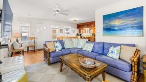 Ein Wohnzimmer mit einem blauen Sofa, einem Holztisch und einem Gemälde von einem Sonnenuntergang.