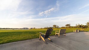 Une zone pavée avec deux fauteuils Adirondack donnant sur un champ d’herbe et un bâtiment situé au loin.