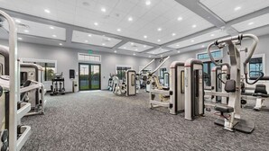 Une salle de sport moderne équipée de divers appareils d’exercice, dotée d’un sol recouvert de moquette et d’une grande fenêtre laissant entrer la lumière naturelle.