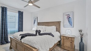 Une chambre à coucher avec un lit en bois, du linge de lit blanc, un ventilateur de plafond et des œuvres d’art accrochées aux murs.