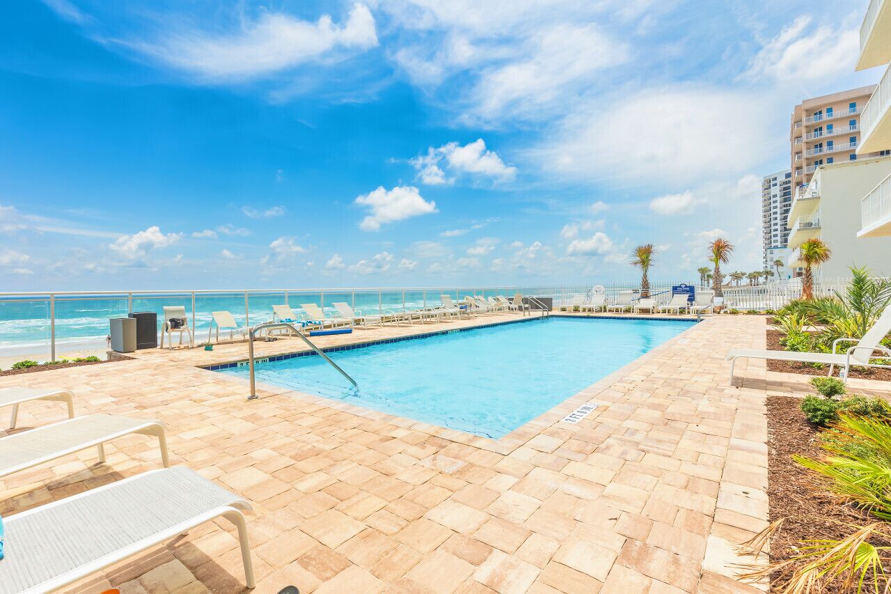 A pool area with lounge chairs and a view of the ocean.