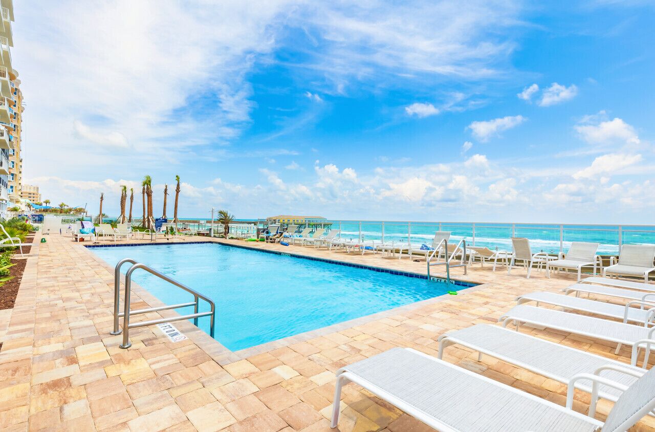 A pool area with lounge chairs and a view of the ocean.