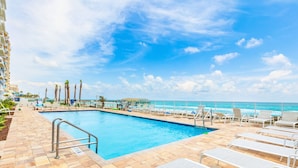 A pool area with lounge chairs and a view of the ocean. - A Wave From it All Oceanfront Pool Condo (Daytona Beach Shores)