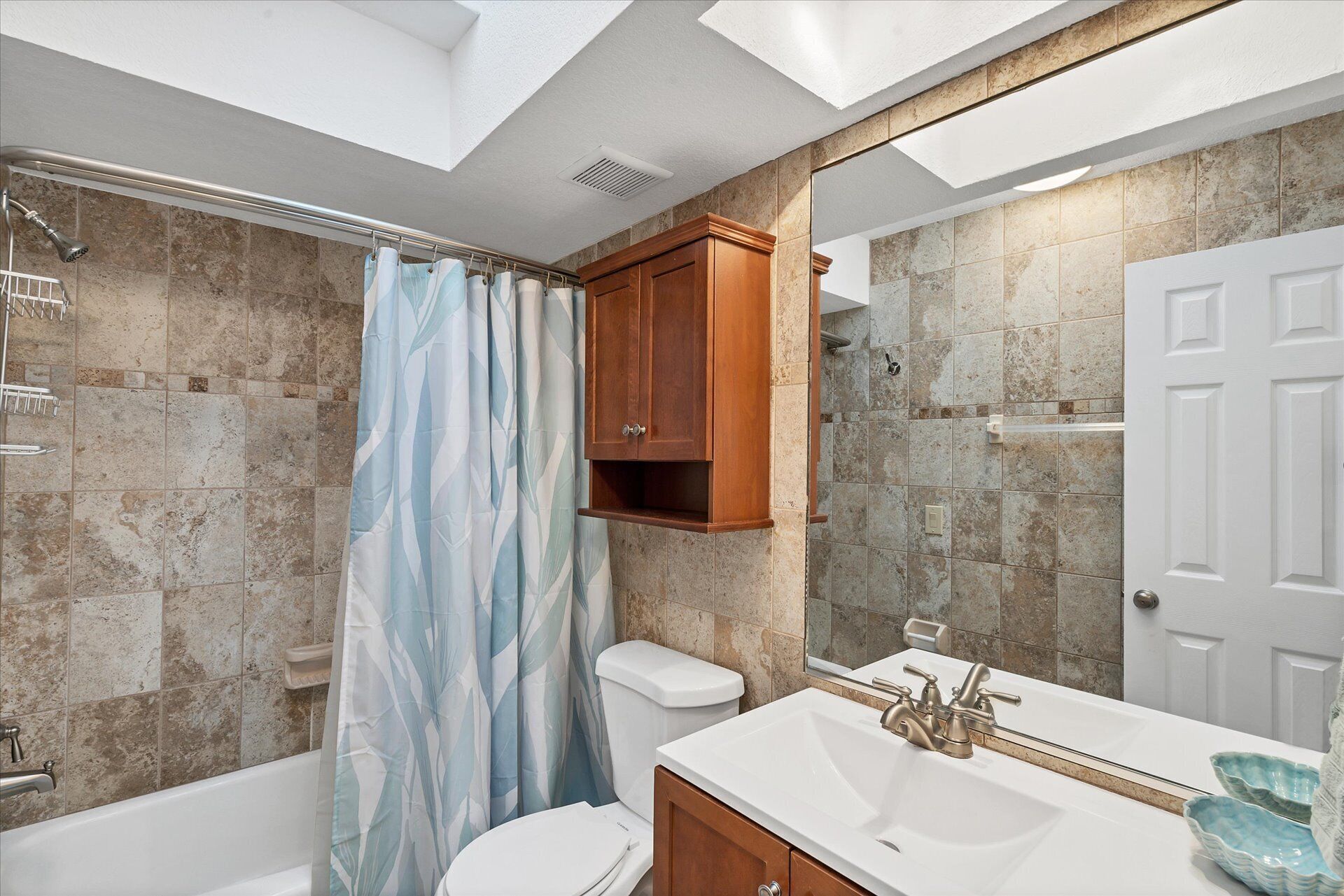 Un bagno con finestra a soffitto, doccia, servizi igienici, lavabo e mobiletto in legno.