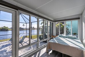 Quarto com grandes janelas com vista para um corpo d'água, uma cama e área de varanda com cadeiras.