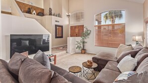 A spacious living room with a large sofa set, a flat-screen TV, a staircase, and a large window with blinds. - Family Fun in Ahwatukee Phoenix (Phoenix)