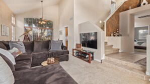 A spacious living room with a large sectional sofa, a flat-screen TV, and a staircase leading to an upper level. - Family Fun in Ahwatukee Phoenix (Phoenix)