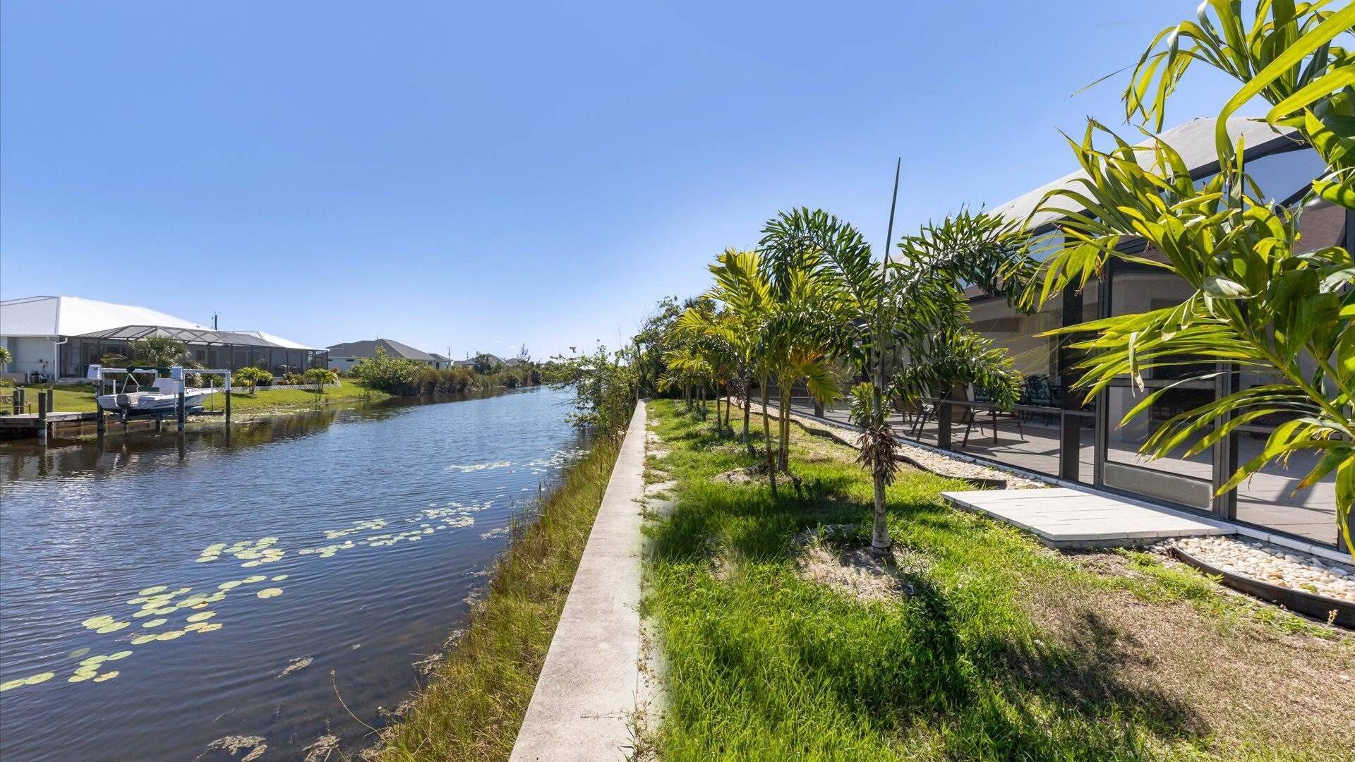 A canal with water lilies, a concrete walkway, and buildings with large windows.
