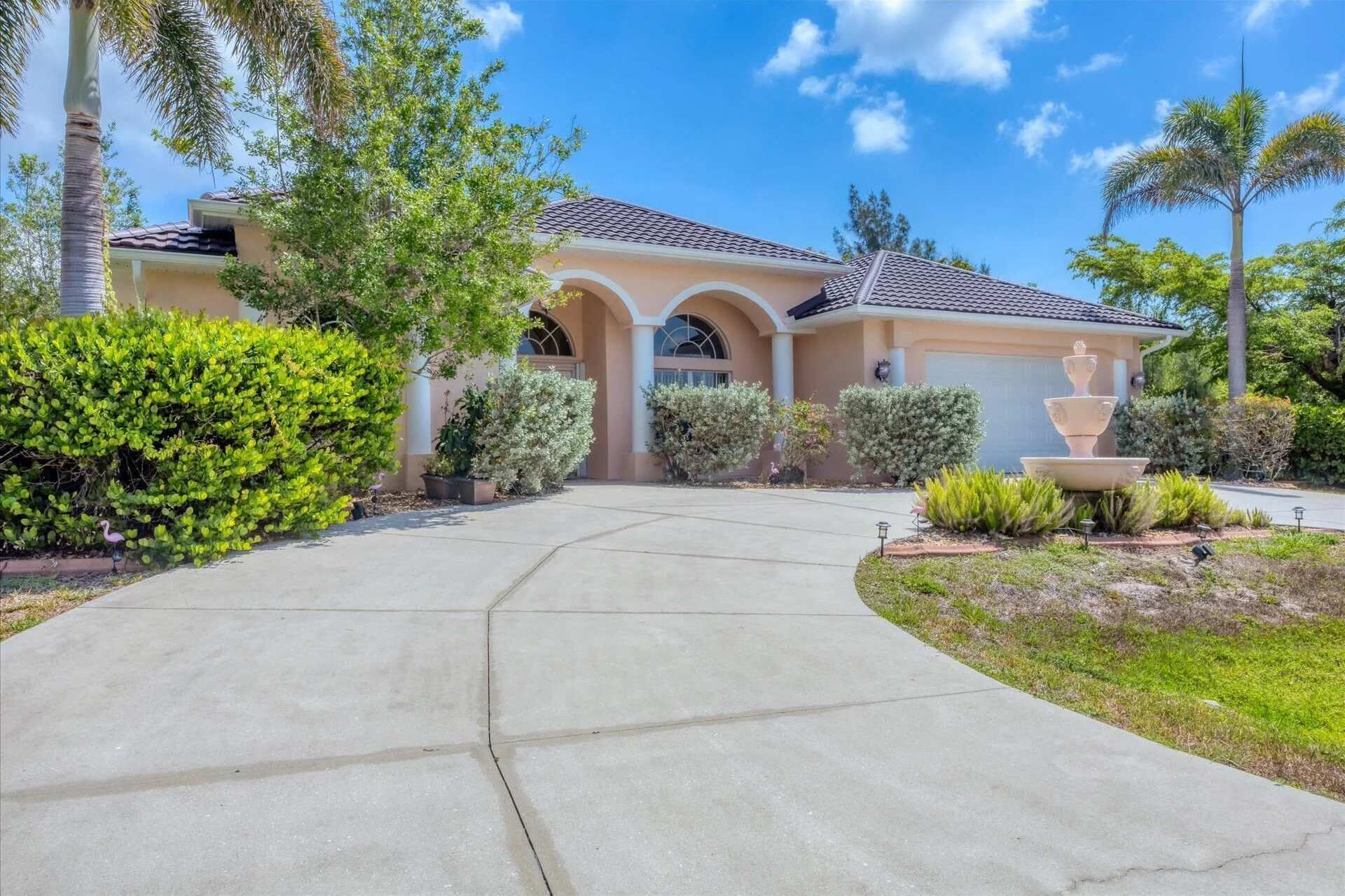 A residential house with a curved driveway, a fountain, and well-maintained landscaping.