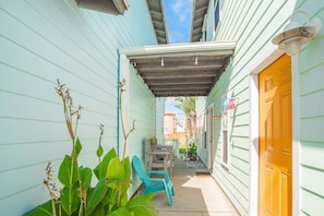 A narrow outdoor corridor with a covered patio area, a wooden table, and two chairs. - Another Day in Paradise - Beach Gear Credit Included! (Port Aransas)