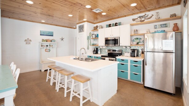Een keuken met een centraal eiland, houten plafond, blauw-witte kasten en een koelkast van roestvrij staal.